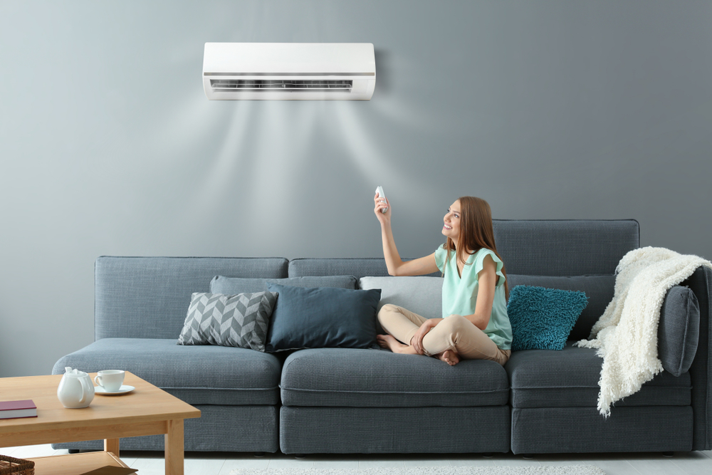 Young,Woman,Switching,On,Air,Conditioner,While,Sitting,On,Sofa